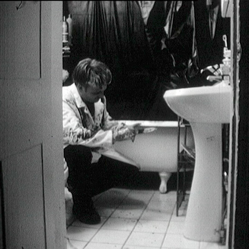 Photo of a man covered in blood holding a knife in a bathroom